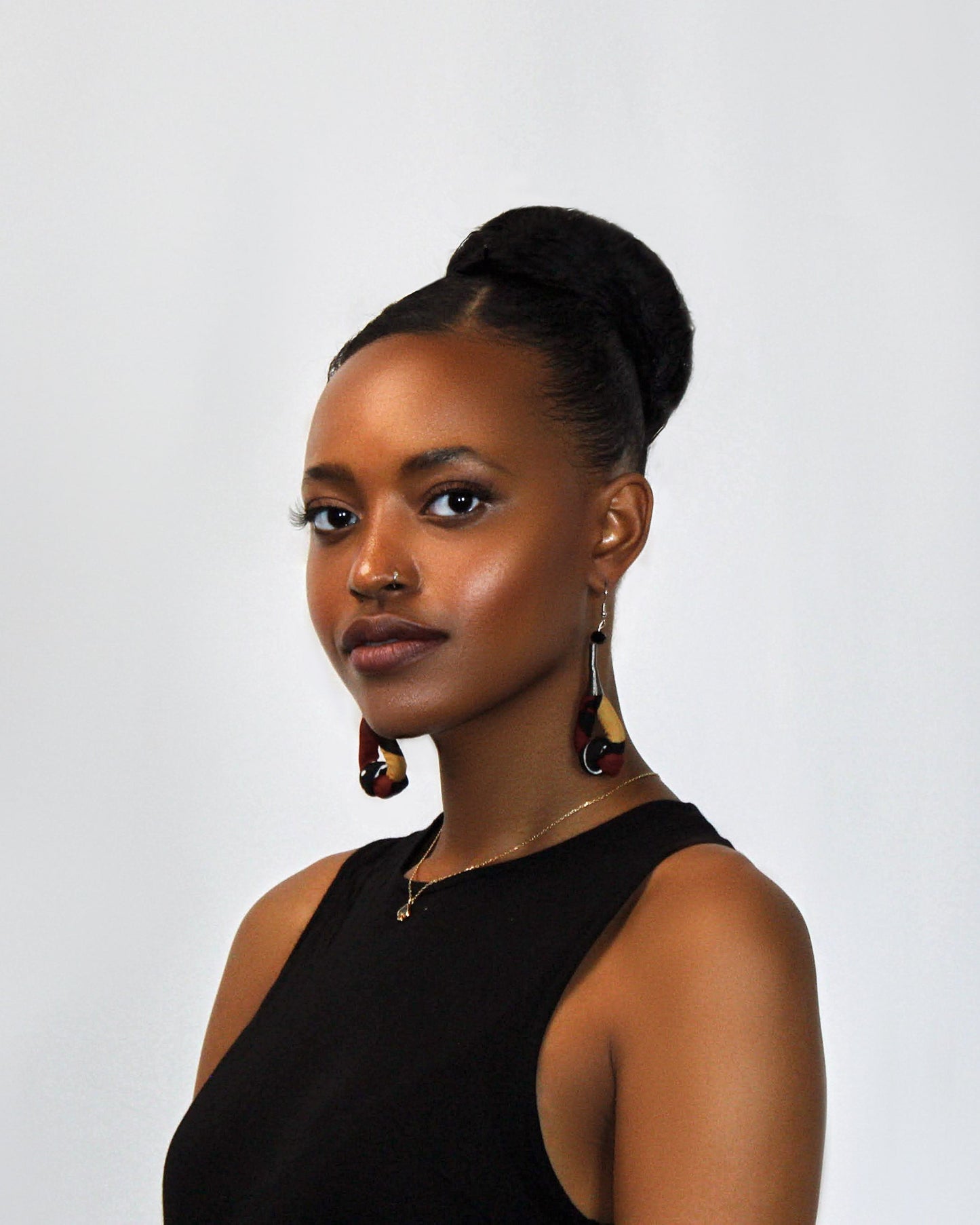 Woman wearing hand crafted fabric earrings in red, black and mustard yellow print, wearing a black top against a plain background